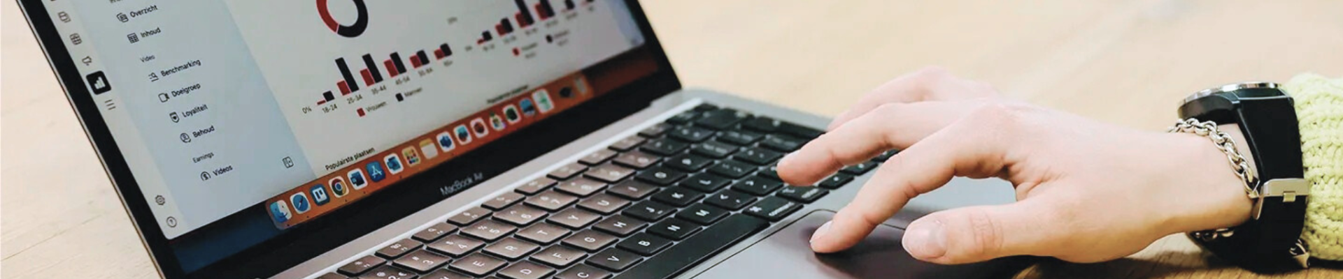 Laptop op houten tafel toont data en hand op toetsenbord klikt iets aan in kantooromgeving.