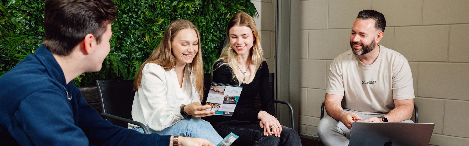 Vier lachende personen zittend rondom een salontafel met flyers in hun hand.