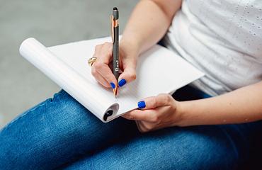 Hand die pen vasthoudt en iets schrijft op blad van notitieblok.
