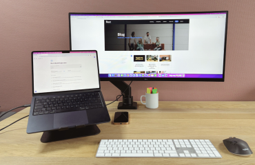 Bureau met daarop laptop op standaard en brede monitor daanaast.