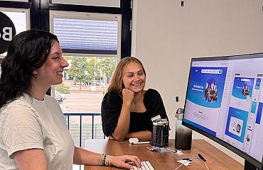Twee collega’s werken samen achter een bureau terwijl ze een websiteontwerp op het computerscherm bekijken.