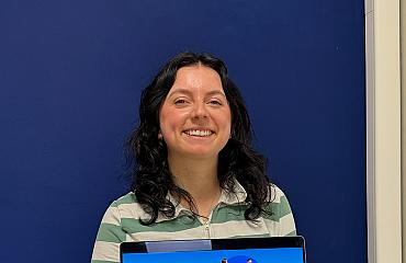 Een collega houdt glimlachend een laptop omhoog waarop de tekst “Wij helpen jou gewoon met je marketing” zichtbaar is.