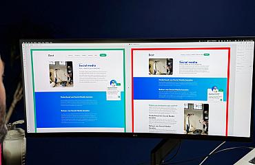 Een man bekijkt twee webdesigns naast elkaar op een ultrabrede monitor in een kantooromgeving.