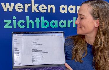 Vrouw houdt laptop met AI-tekst op scherm voor blauwe achtergrond met tekst 'werken aan zichtbaarheid'.