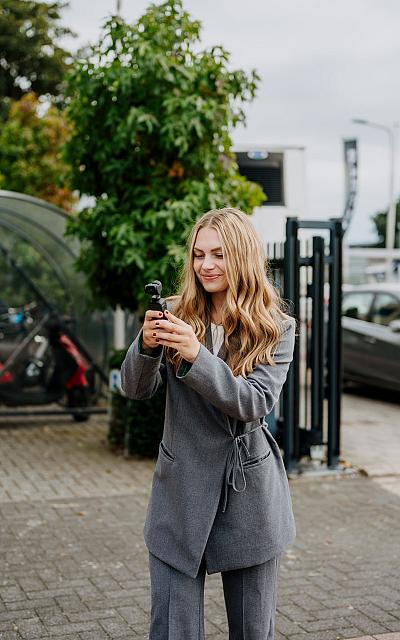 Vrouw die lachend een selfie maakt met haar telefoon in een zwarte hoes met het logo van Best Marketingbureau, zittend op een bruine bank.