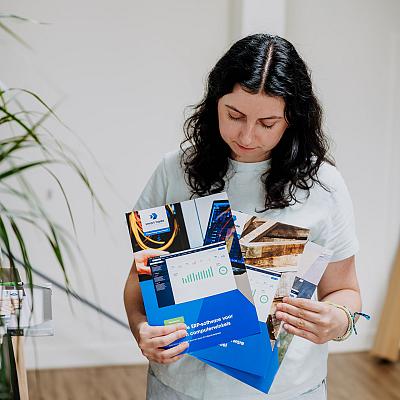 Vrouw bekijkt enkele kleurrijke brochures van Smart Trade met grafieken en bedrijfsfoto’s, terwijl ze in een lichte kantoorruimte staat.
