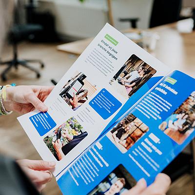 Close-up van iemand die een kleurrijke brochure van Smart Trade bekijkt in een modern kantoor.