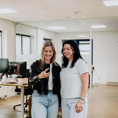 Beeldscherm met het ontwerp van het logo van Best Marketingbureau in Adobe Illustrator, met op de achtergrond een vrouw die op kantoor aan haar bureau zit.