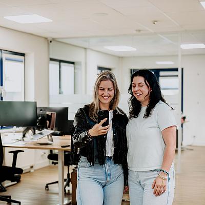 Beeldscherm met het ontwerp van het logo van Best Marketingbureau in Adobe Illustrator, met op de achtergrond een vrouw die op kantoor aan haar bureau zit.