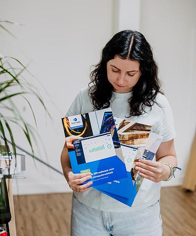 Vrouw bekijkt enkele kleurrijke brochures van Smart Trade met grafieken en bedrijfsfoto’s, terwijl ze in een lichte kantoorruimte staat.