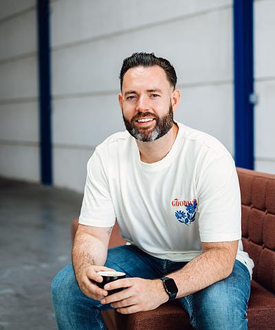 Man die ontspannen op een bank zit met een kop koffie in zijn handen, in een lichte industriële ruimte met blauwe accenten.