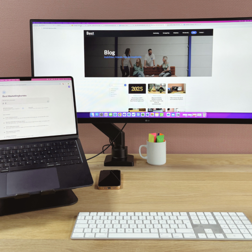 Bureau met daarop laptop op standaard en brede monitor daanaast.
