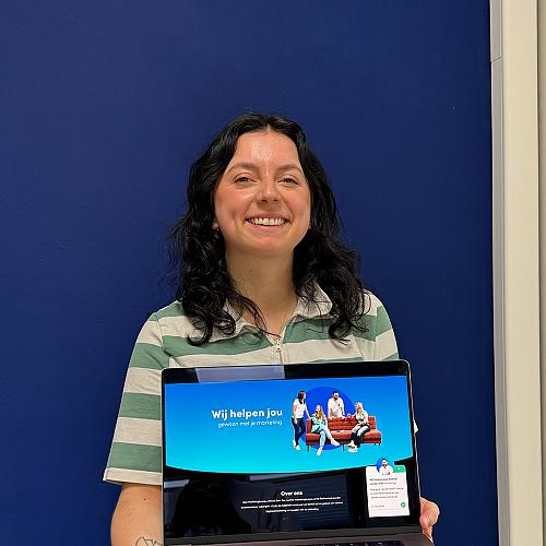 Een collega houdt glimlachend een laptop omhoog waarop de tekst “Wij helpen jou gewoon met je marketing” zichtbaar is.