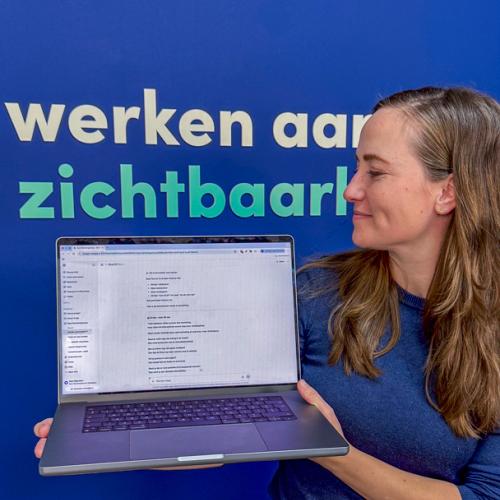 Vrouw houdt laptop met AI-tekst op scherm voor blauwe achtergrond met tekst 'werken aan zichtbaarheid'.