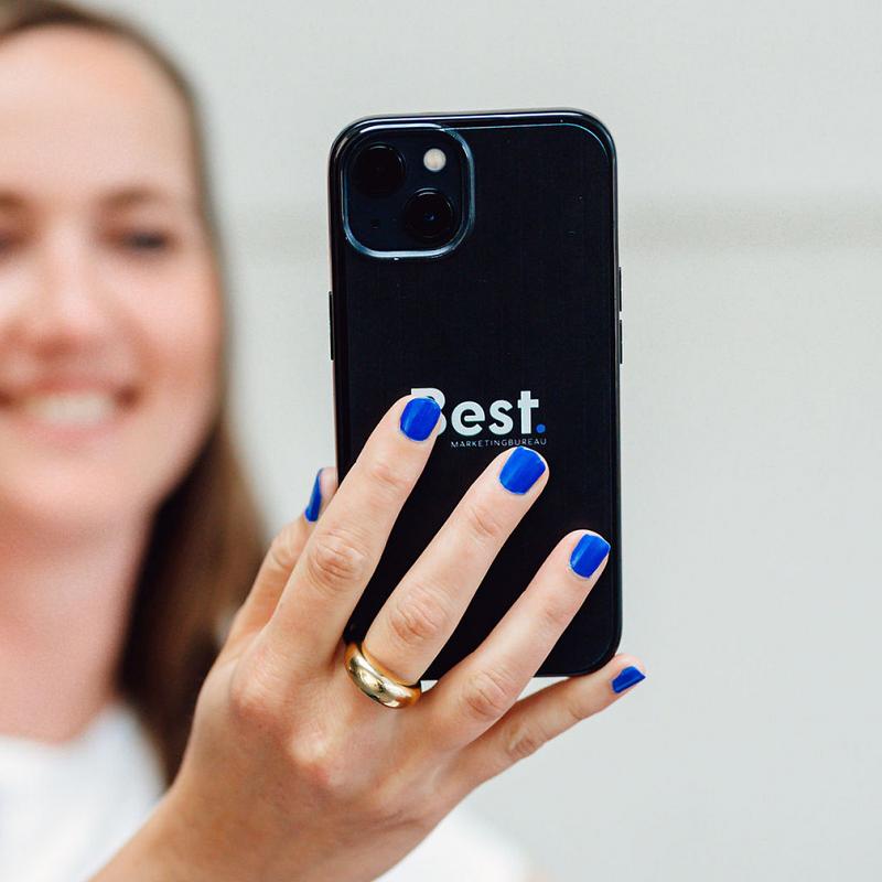 Vrouw maakt een foto met haar smartphone met het logo van Best Marketingbureau op de achterkant.