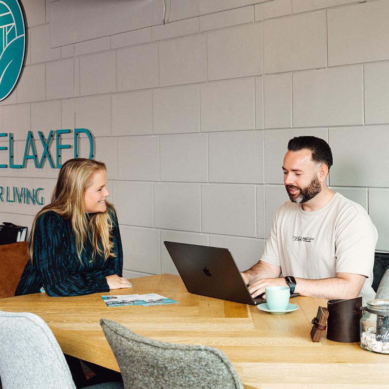 Twee mensen bespreken samen werk aan tafel terwijl ze naar een laptop kijken.