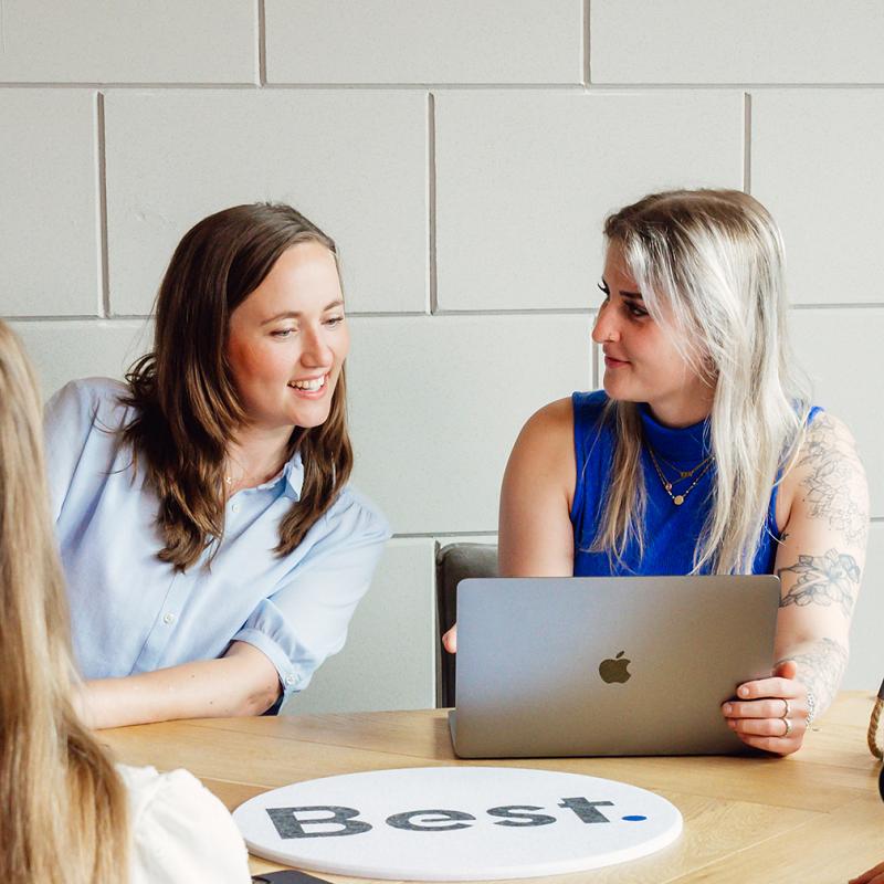 Twee collega’s overleggen aan tafel terwijl ze samen naar een laptop kijken.